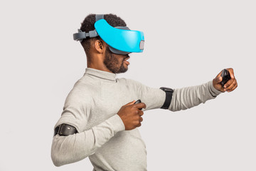 Amazed excited African businessman in white sweater using mobile vr headset, experiencing virtual reality while playing video game against white wall.