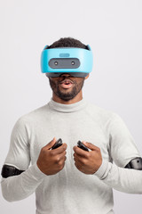 African male gamer experiencing boxing game with VR goggles, headgear and 3D simulation through virtual reality glasses isolated over grey background.