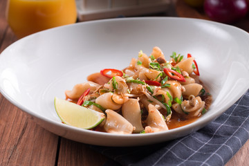 The traditional Asian dish is grilled squid with spicy paprika and tomatoes. wooden background