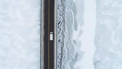 White car rides on highway across frozen lake view from above