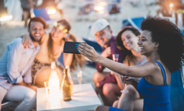 Happy friends taking selfie with smartphone at beach party outdoor - Young people having fun together at bar drinking champagne  - Focus on african girl hand phone - Youth and summer concept