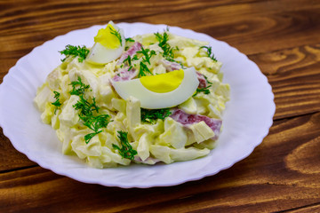 Salad with chinese cabbage, onion, sausage, eggs and mayonnaise on wooden table