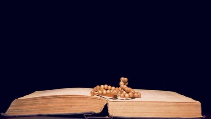 Wooden rosary falling on a Bible.