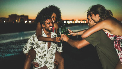Happy friends drinking beer and having fun on the beach after sunset - Soft focus on left guys faces