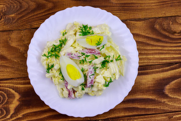 Salad with chinese cabbage, onion, sausage, eggs and mayonnaise on wooden table