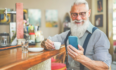 Happy senior man using smartphone app while drinking coffee inside vintage bar