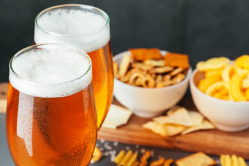 Glass of lager beer with snack bowls on dark stone background