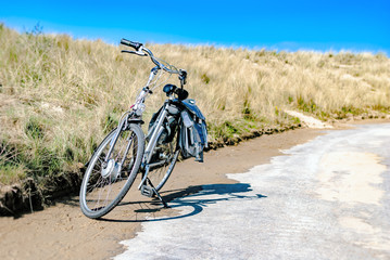 Fototapeta premium A bicycle parked along a coastal road with dunes at the background. Summer concept. Vacation. Bike rental. Biking. Tourism. Retreat. Spring. Nature therapy. Vlissingen, the Netherlands. Northern sea.