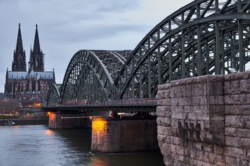 Der berühmte Blick auf die Wahrzeichen von Köln bei Tag. Über die Hohenzollernbrücke fahren täglich hunderte Züge und tausende Menschen, während sie den Ausblick auf das Kölner Panorama genießen.