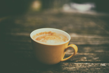 A yellow cup of tasty coffee, on rustic wooden table background