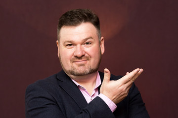 A middle-aged man, a large portrait. A man with a beard in a suit on a dark background raised his hand to his chin.