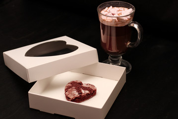 hot drink in a glass cup with pink marshmallows and white box with a transparent cover in the form of heart with cookies