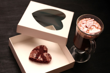 hot drink in a glass cup with pink marshmallows and white box with a transparent cover in the form of heart with cookies