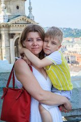 Fototapeta na wymiar Concept of joyful journey with children. Happy mother and wonderful son smiling look at camera and standing on observation deck of St. Stephen's Basilica in Budapest, Hungary.
