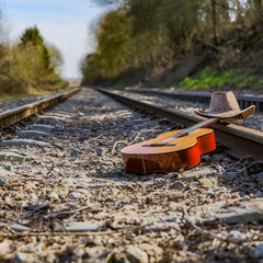 Guitar and a hat on the old train tracks between trees with a sense of depth, sunny and quiet day in the Netherlands. Reflection, abandono and travel concept
