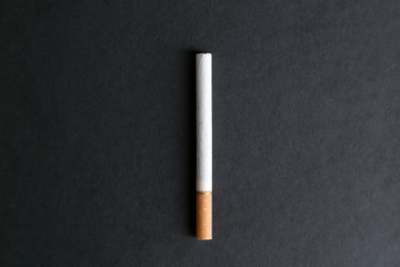 A cigarette with a filter on a black background. A large whole cigarette with tobacco on a uniform background. Place for inscription.