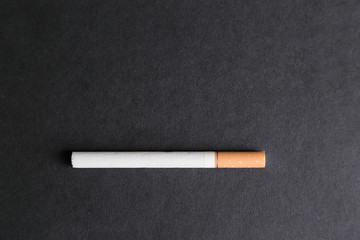 A cigarette with a filter on a black background. A large whole cigarette with tobacco on a uniform background. Place for inscription.