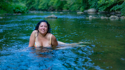 Beautiful latin woman with long black hair enjoying a wonderful summer day in the Ahr river in Schuld Germany with green vegetation on a blurred background