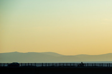 Fototapeta premium Motorcycle on the highway bridge during the dawn against the backdrop of mountains and the sea