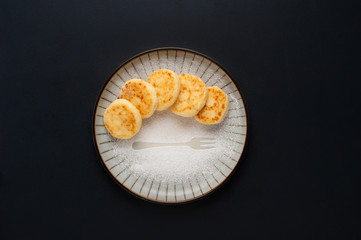 Cottage cheese pancakes on a plate on the dark background.