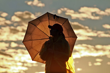 Silhouette girl with umbrella on the background of incredible sunset, sky and clouds