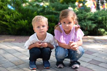 Small children, girl and boy, brother and sister, squat and carefully look at the camera, waiting...