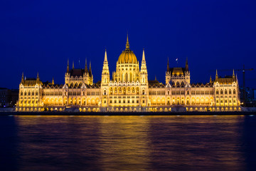 Illuminated Budapest parliament building at night with dark sky and reflection in Danube river