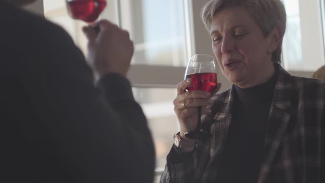 Back of man with glass of red wine and portrait of happy smiley senior woman with grey short hair with glass of wine. Couple talk and enjoy time together. Happy family. S-log, ungraded