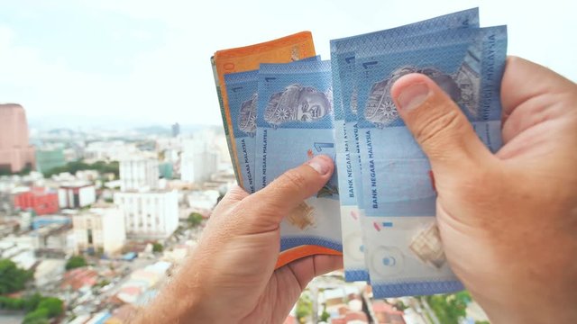 A young man recounts in his hands the money of Malaysia against the background of the city center of Kuala Lumpur.