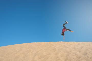 young asian male make an acrobatic backflip moves on a sand dune. concept of freedom, happiness, travel and active lifestyles