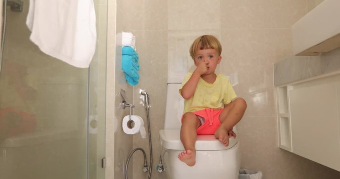 Child sitting toilet with thoughtful look picks his nose