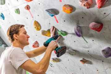 Rock climber fastens the hook with a screwdriver at the climbing wall in the boulder hall © Baikal360