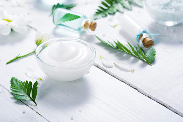 spa setting with cosmetic cream, gel, bath salt and fern leaves on white wooden table background