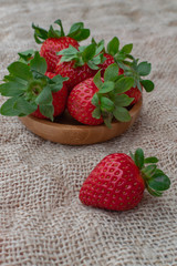 Ripe strawberries in a wooden bowl, and on sack surface