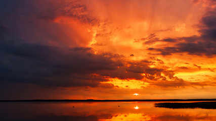 Stunning panorama of an unusually beautiful sunset with amazing sky over the lake on a warm summer day