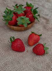 Ripe strawberries in a wooden bowl, and on sack surface