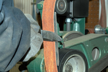 The knife maker shapes and sharpens the newly constructed blade. Bokeh background.