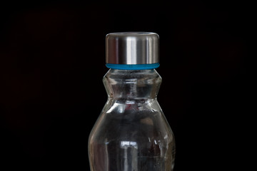 An empty glass water bottle isolated against a black background image with copy space
