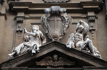 Statues of Hope and Poverty seated either side of the arms of the Theatine order over the central door on the facade of Santi Michele e Gaetano church in Florence, Italy