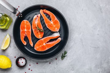 Fresh raw salmon steaks with lemon and rosemary in grill pan on gray background.