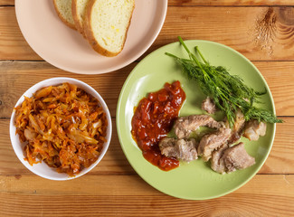 Pieces of roast meat, tomato sauce, dill bread and sauerkraut on a plate on the table.