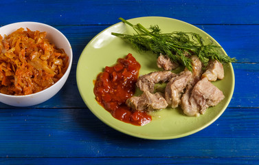Pieces of roast meat, tomato sauce, dill bread and sauerkraut on a plate on the table.