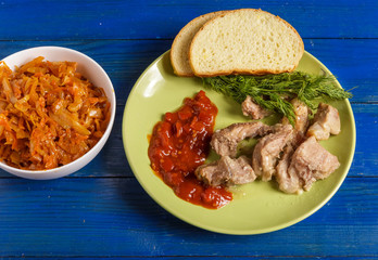 Pieces of roast meat, tomato sauce, dill bread and sauerkraut on a plate on the table.