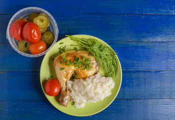 Fried chicken leg, dill, rice and tomato on a plate on the table.