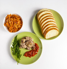Pieces of roast meat, tomato sauce, dill bread and sauerkraut on a plate on a white background.