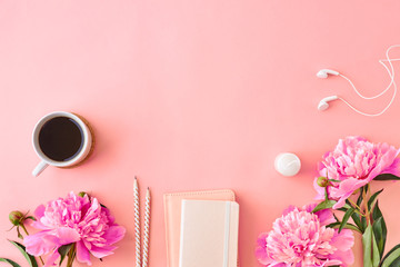 Flat lay blogger or freelancer workspace with a notebook and pink peonies on a pink background