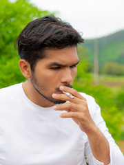 Young man smoking cigarette in the outdoors and nature background.