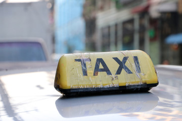 Taxi light sign or cab sign in yellow color with black text and tied with transparent tape on the car roof at the street blurred background.