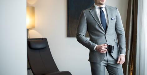 Man model in expensive custom tailored suit holding a cup of coffee in hand while standing