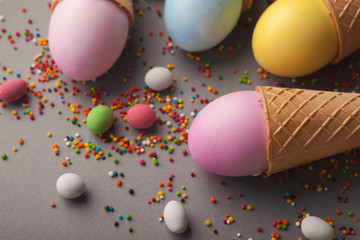 Colorful easter eggs in waffle cones on gray background